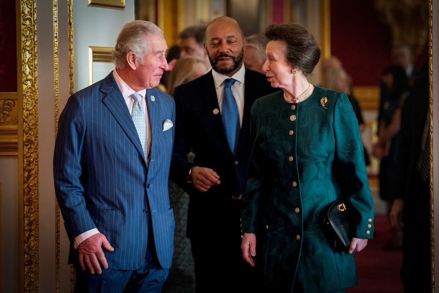 King Charles and Princess Anne grinning at each other while walking into a room 