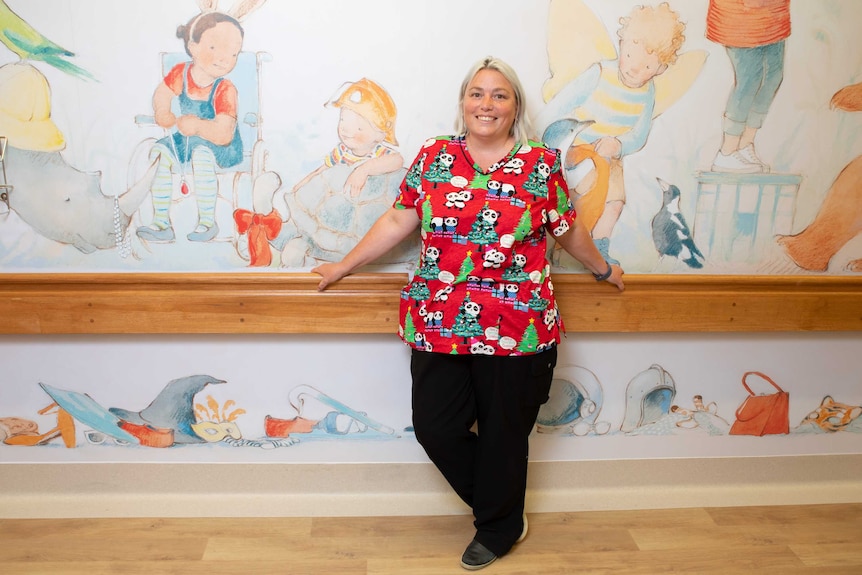 Donna stands in front of a mural on the ward, smiling, wearing a top with pandas on it.