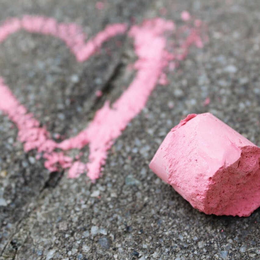 Photo of a love heart drawn on asphalt in pink chalk, with the chalk sitting off to the side 