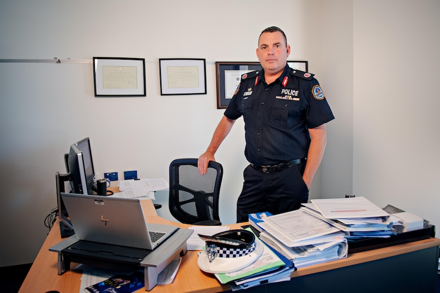 A uniformed police commissioner stands behind his desk in an office.