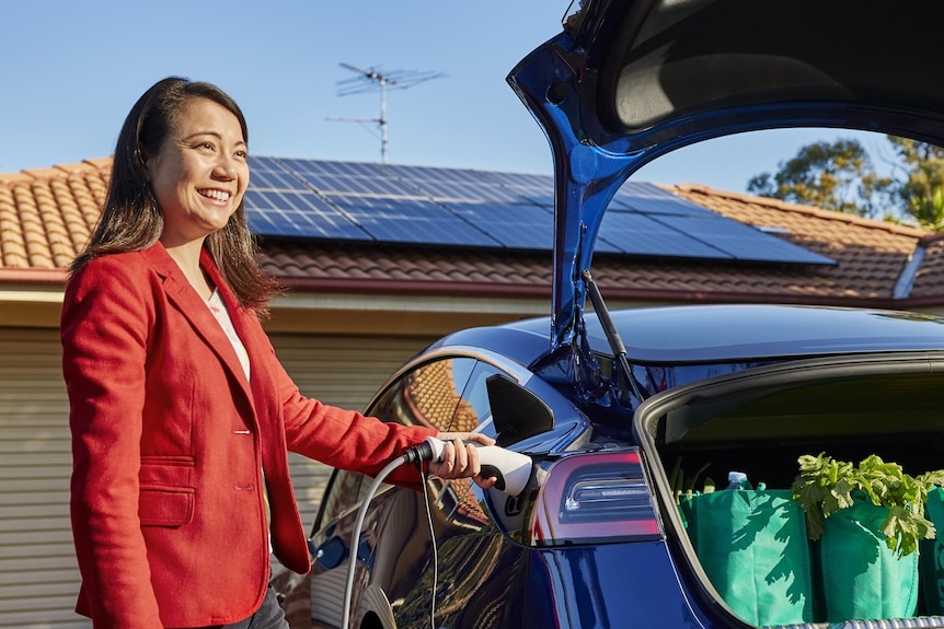 A woman plugs into an electric vehicle.