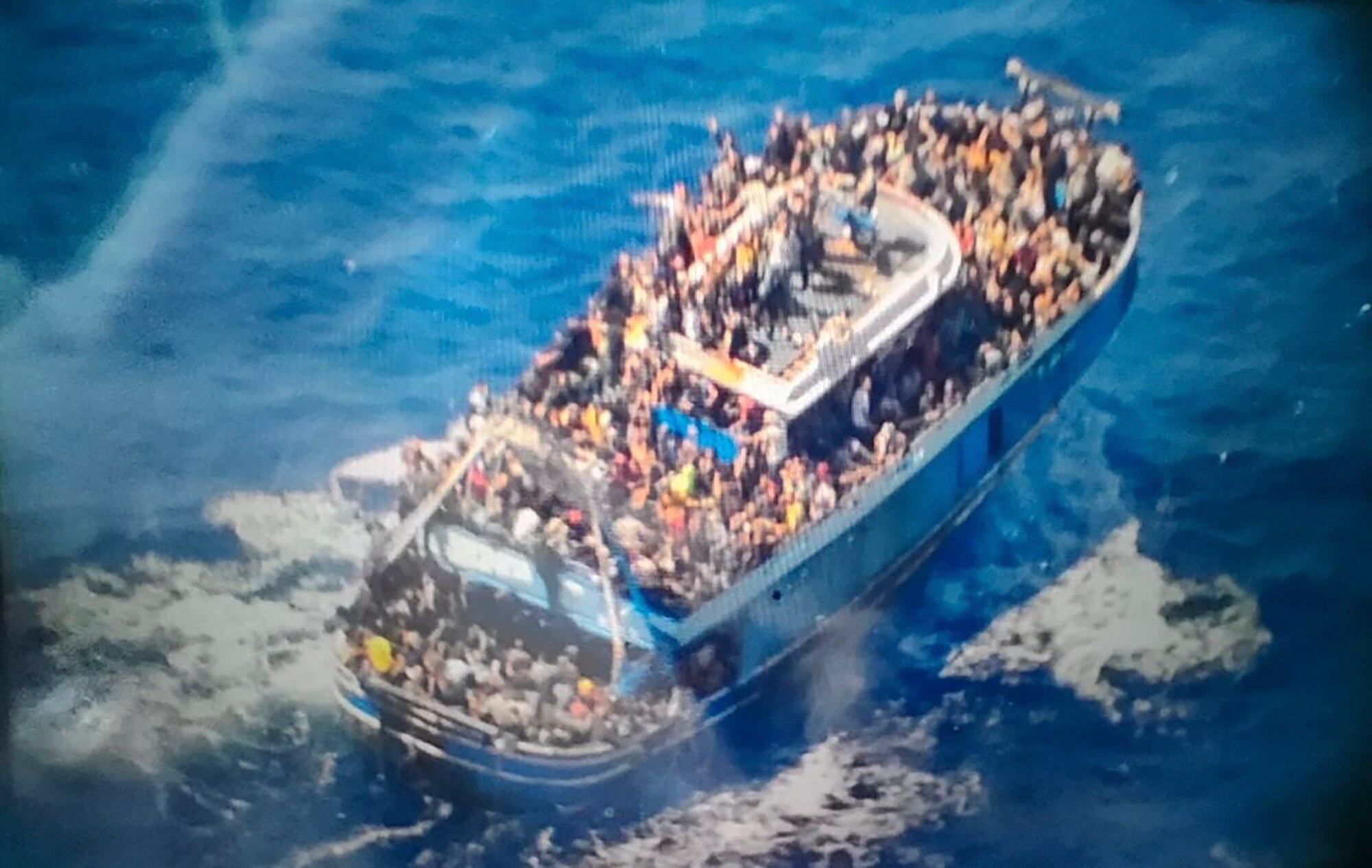 A slightly blurry photo shows hundreds of people crammed onto the deck of a blue fishing boat in the ocean.