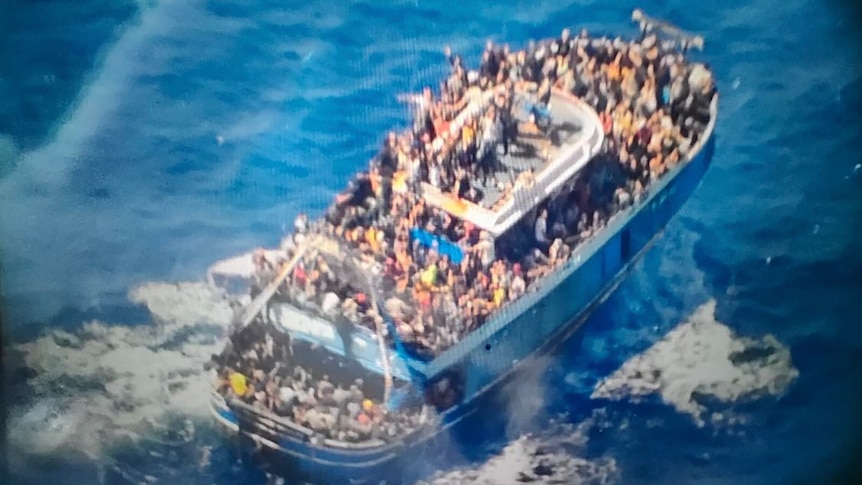 A slightly blurry photo shows hundreds of people crammed onto the deck of a blue fishing boat in the ocean.