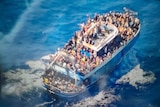 A slightly blurry photo shows hundreds of people crammed onto the deck of a blue fishing boat in the ocean.