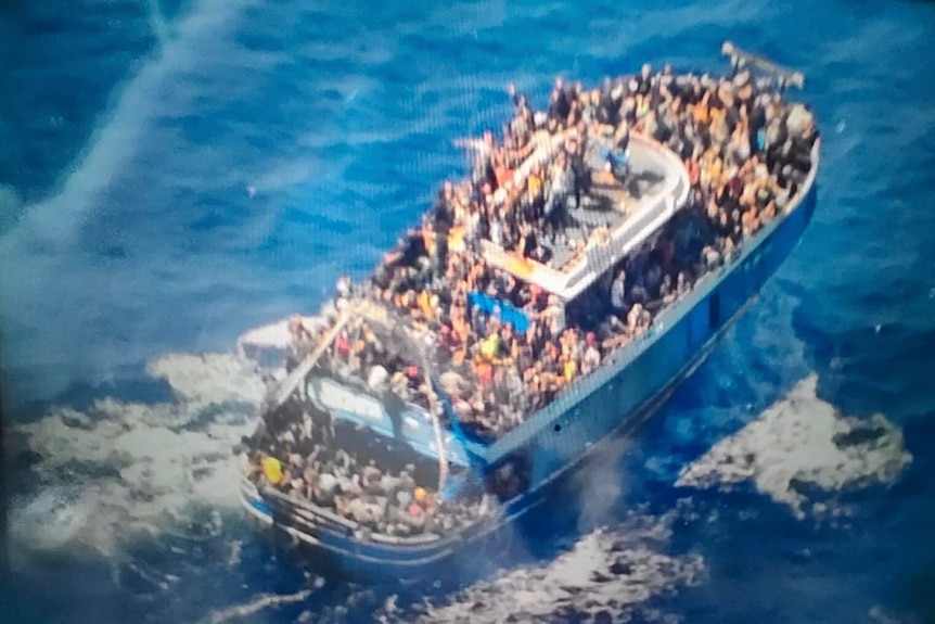 A slightly blurry photo shows hundreds of people crammed onto the deck of a blue fishing boat in the ocean.