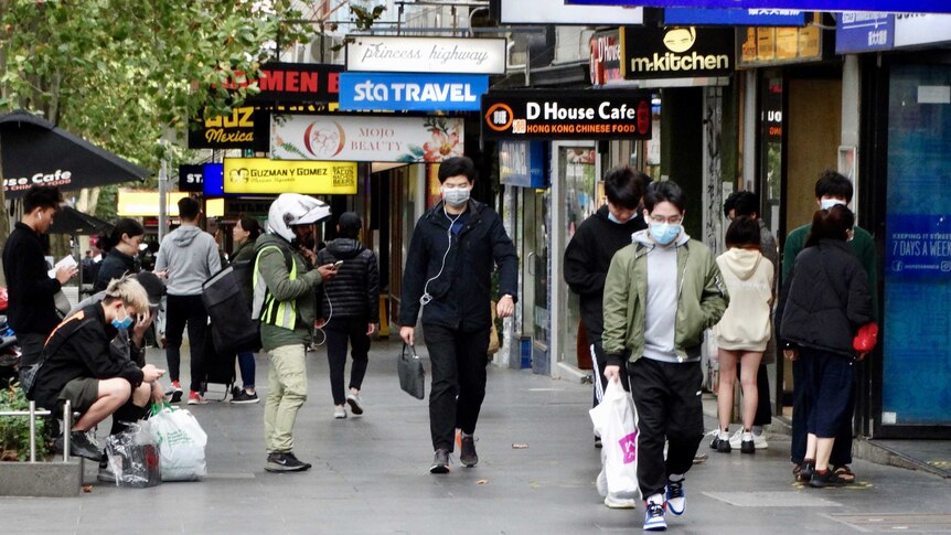 A number of people, some wearing masks, on a busy Melbourne street.
