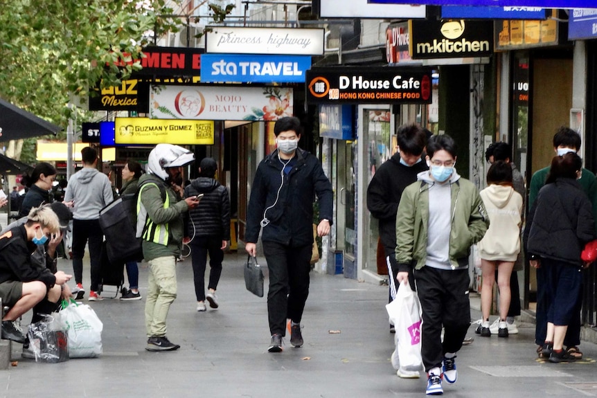 A number of people, some wearing masks, on a busy Melbourne street.