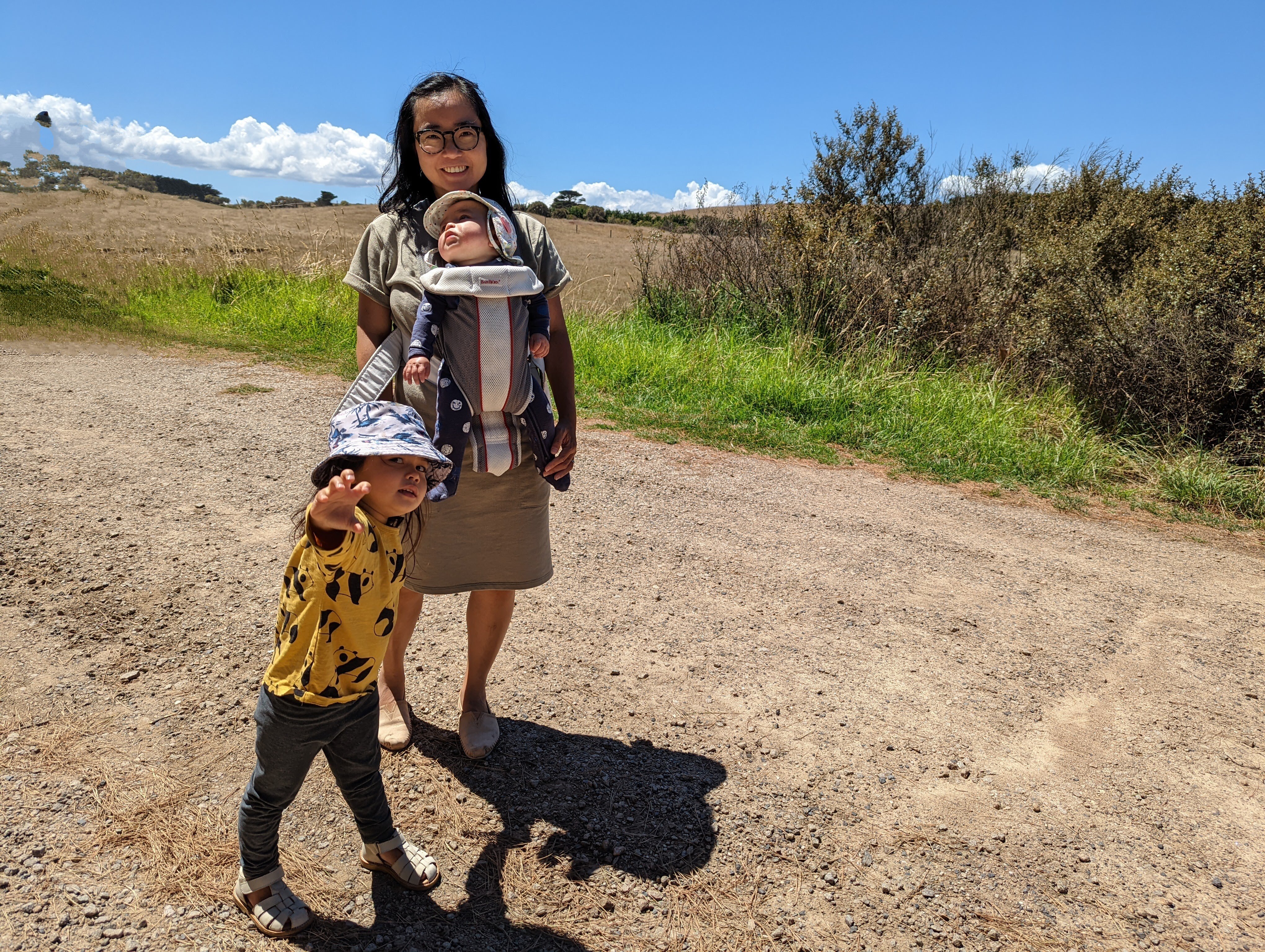 Woman wears baby on her chest in a carrier and a young girl stands at her feet