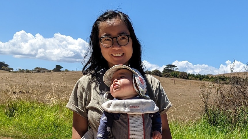 Woman wears baby on her chest in a carrier and a young girl stands at her feet