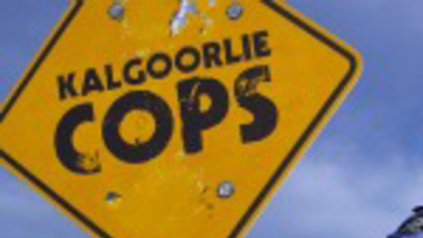 Promotional shot of a Kalgoorlie police officer and car standing next to a sign saying Kalgoorlie co
