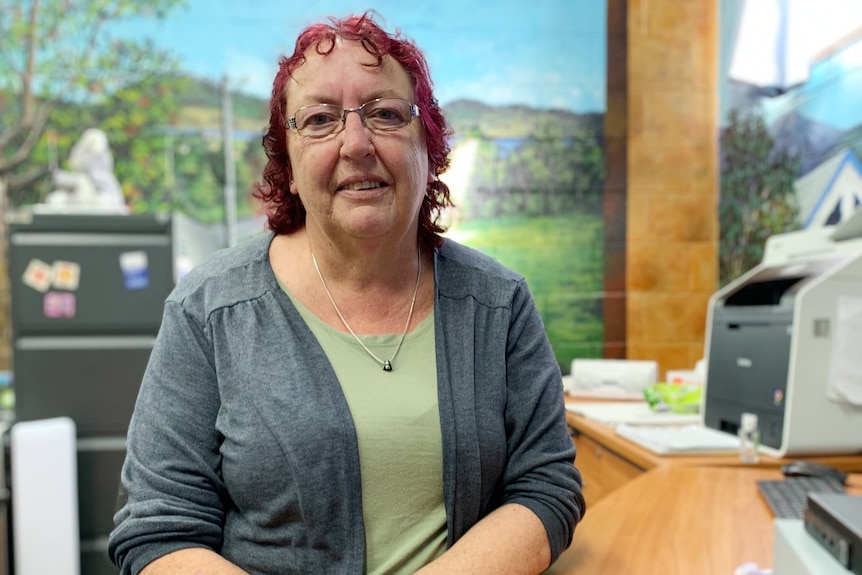 A middle-aged woman with red hair leans on a timber benchtop