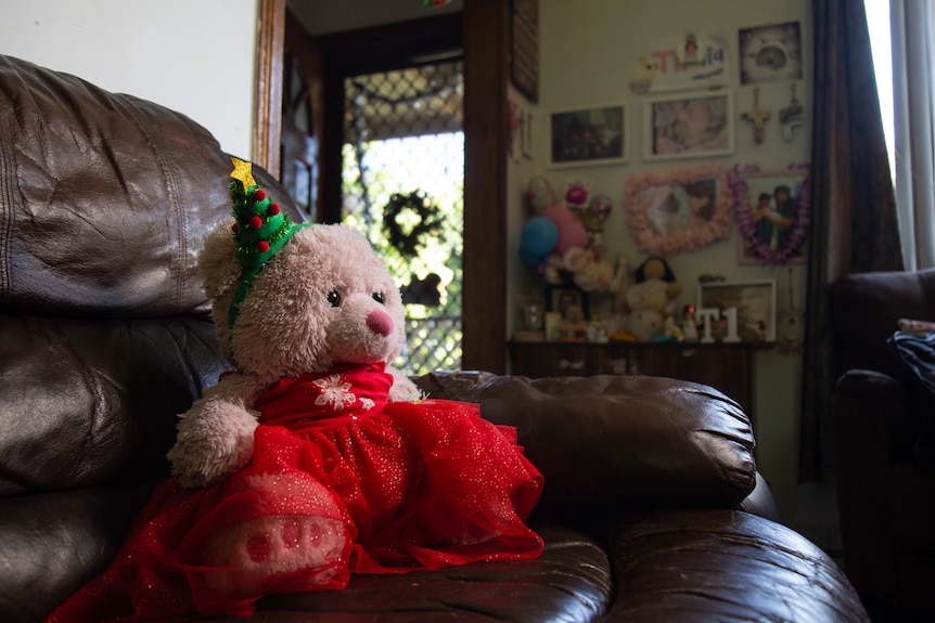 A teddy bear in a red dress sitting on a brown armchair with a Christmas hat.