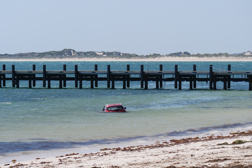 A car appears to be submerged in water with a jetty in the background