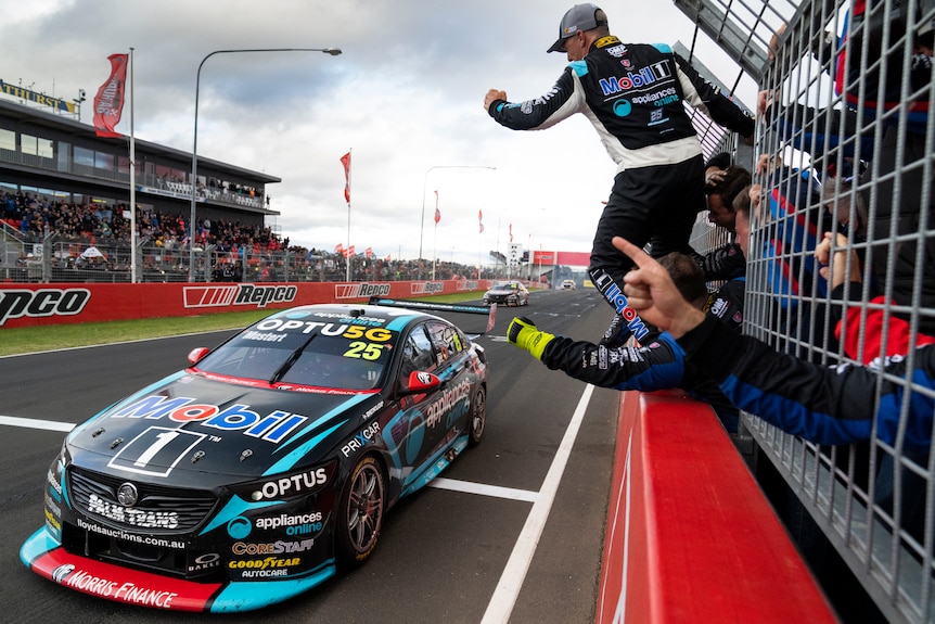 Chaz Mostert drives past his pit wall with people hanging over the fence and clenching their fist