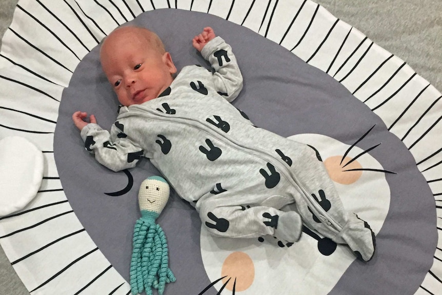 Baby lying on its back on a rug with a small crochet octopus next to it