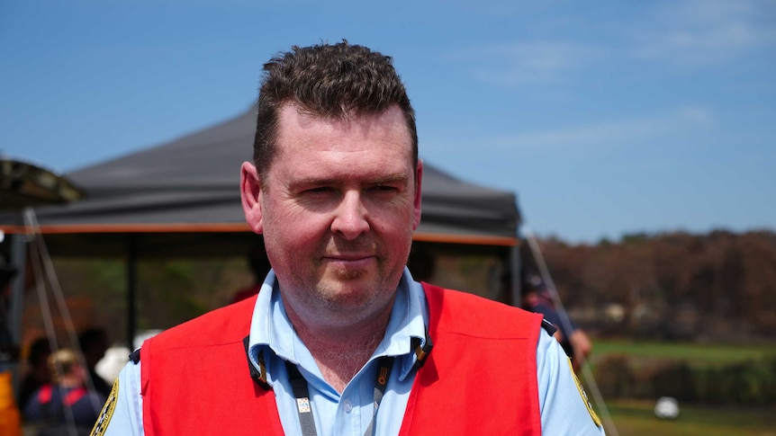 A middle-aged man with short dark hair wearing a high-vis vest looking off camera.