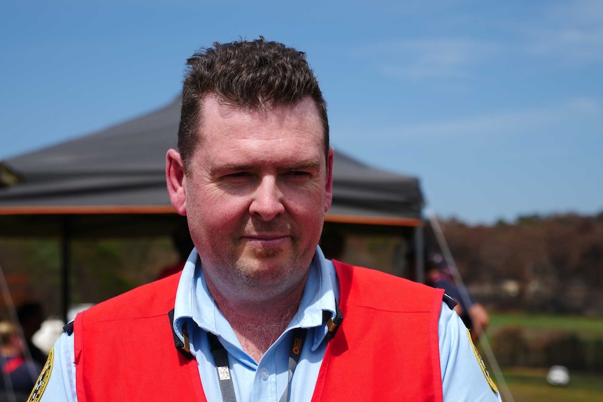 A middle-aged man with short dark hair wearing a high-vis vest looking off camera.