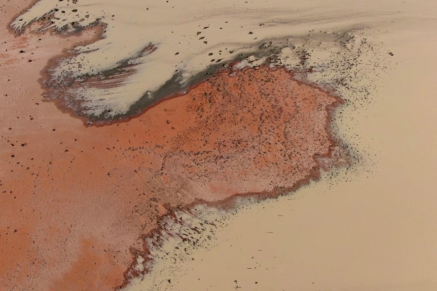 An aerial view of brown water spreading across red earth.
