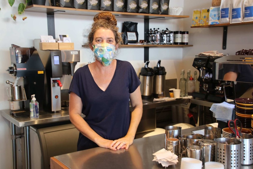 A lady pictured behind a cafe counter wearing a mask.
