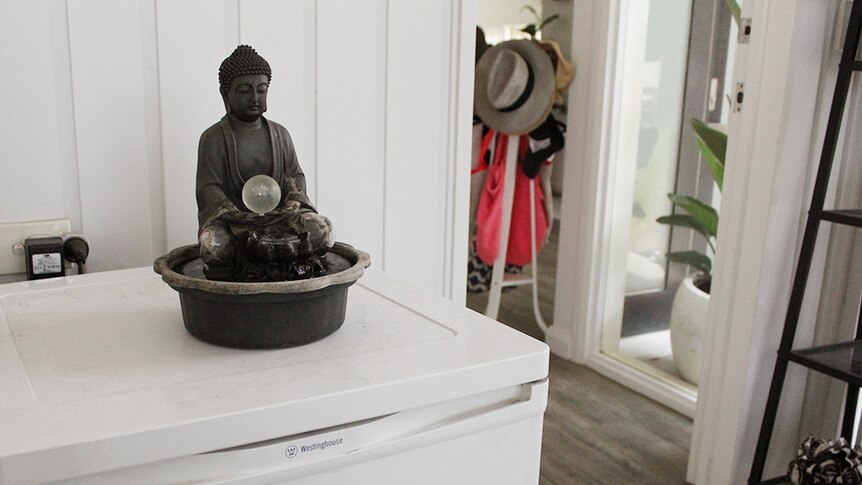 A grey buddha-style water feature sitting on top of a fridge in a garage.
