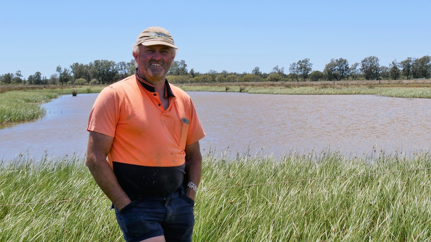 A smiling man in a cap and high-vis stands in front of a wetland.