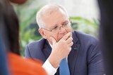 Scott Morrison sitting looking to his left with his hand over his mouth, while he concentrates on something