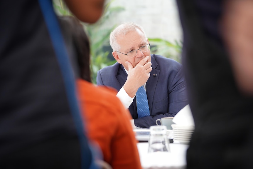 Scott Morrison sitting looking to his left with his hand over his mouth, while he concentrates on something