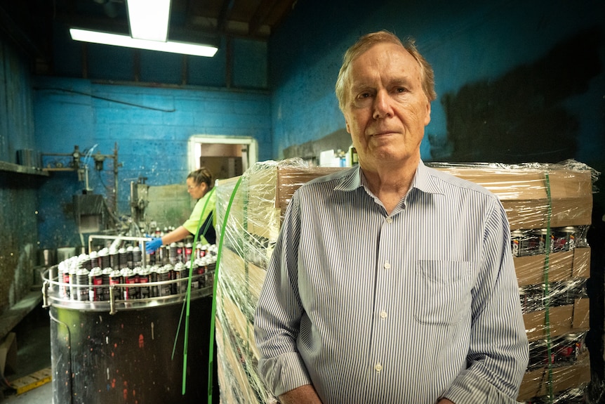 A man stands in a factory where an employee is manufacturing paint.