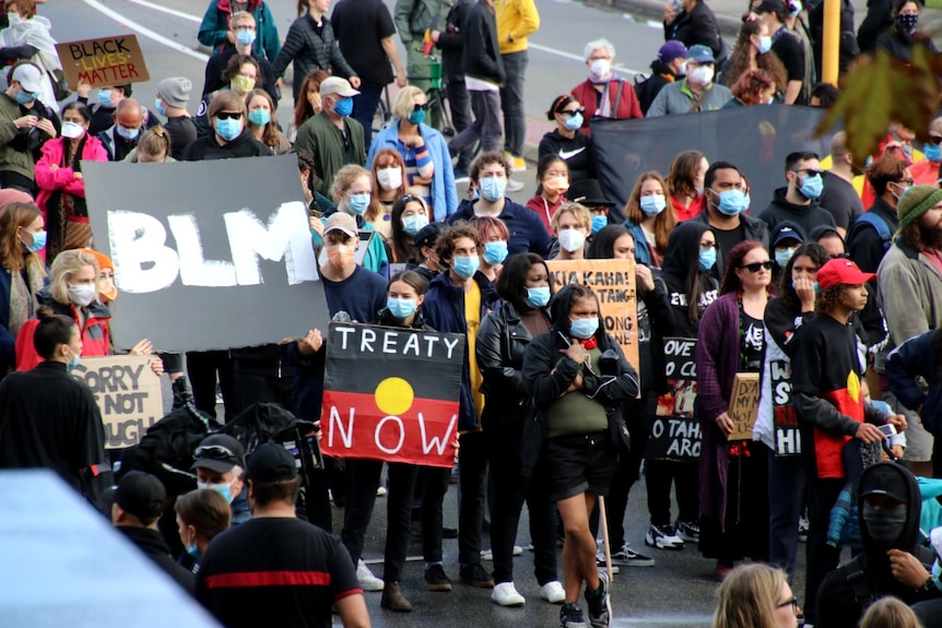 A crowd of people wearing masks and carrying signs walks through the streets of Perth's CBD.