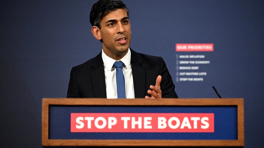 Sunak speaks in front of a lectern emblazoned with the slogan "stop the boats".
