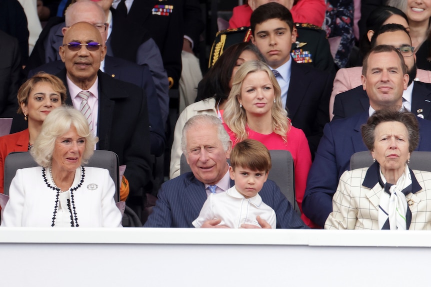Prince Louis sits in the lap of Prince Charles, next to Camilla, Duchess of Cornwall.