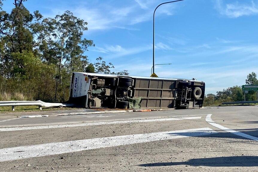 An overturned bus rests on its side beside a road.