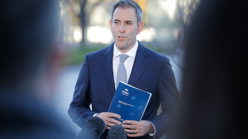 Treasurer Jim Chalmers holds a copy of the 2023-24 federal budget strategy and outlook book in front of the media