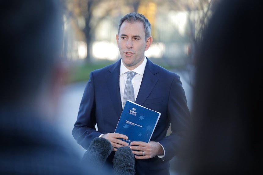 Treasurer Jim Chalmers holds a copy of the 2023-24 federal budget strategy and outlook book in front of the media