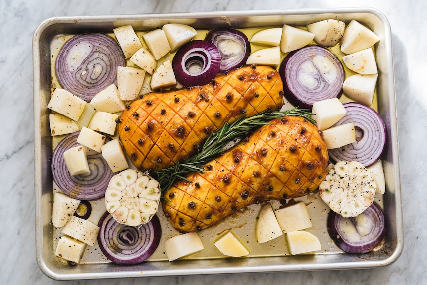 A halved butternut pumpkin with potatoes, garlic and onion roast on a single tray, a vegetarian Christmas recipe idea.