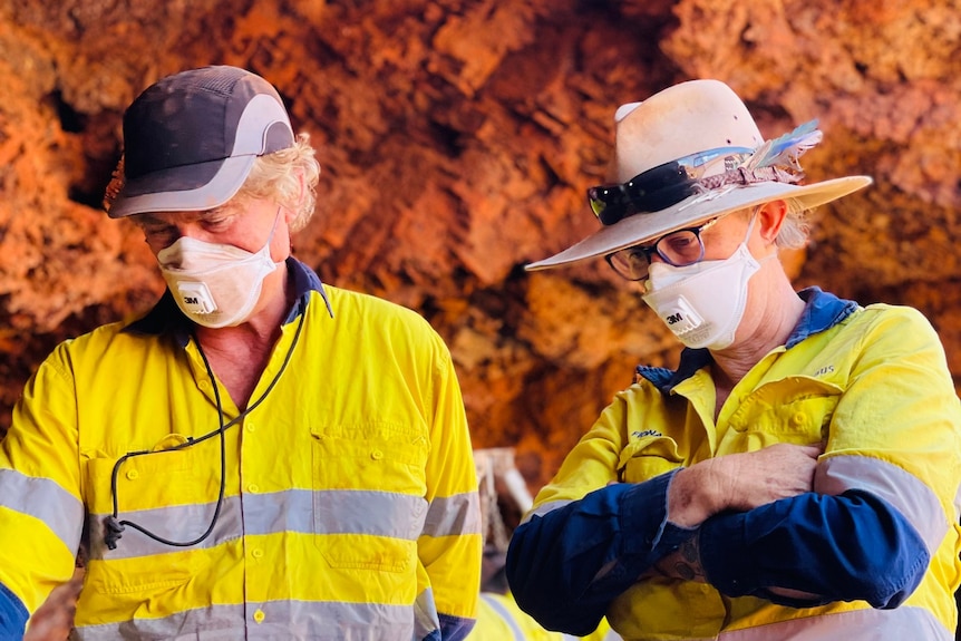 A male and female archaeologist wearing high viz stand under a rock shelter