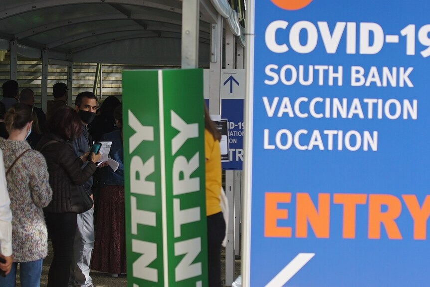A man in a mask near a sign for the South Brisbane vaccination hub.