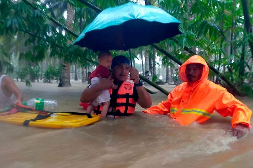 A rescuer carries a child through chest-high brown floodwaters.