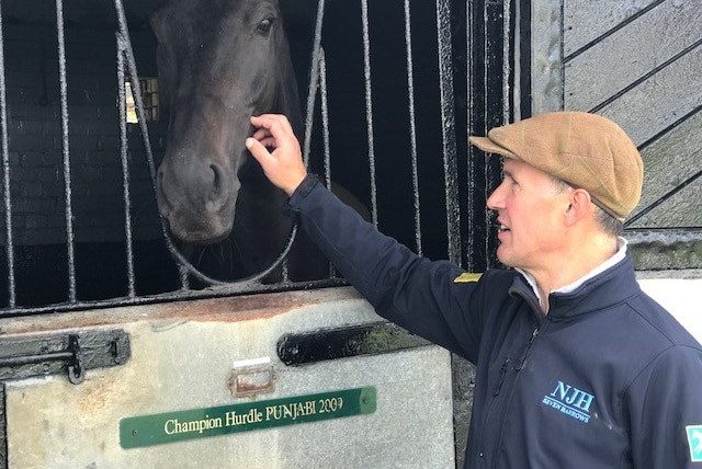 A man pats a horse through a stable door.