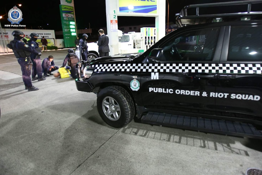 Police officers arrest a man on the ground at a petrol station