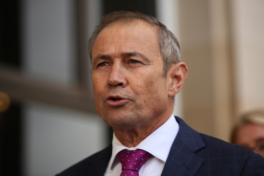 A man in a suit and tie speaks at a press conference. 