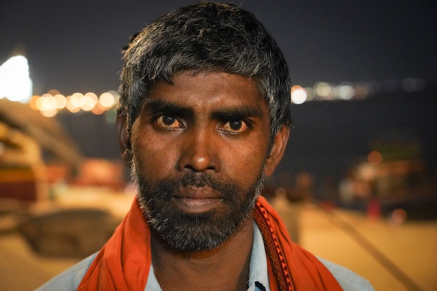 A close up of an Indian man staring at the camera in front of a river.