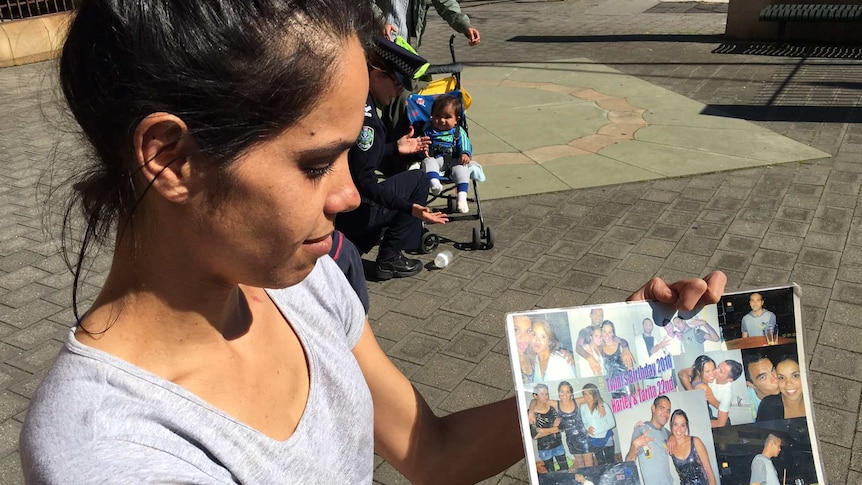 A woman holds photos up toward cameras.