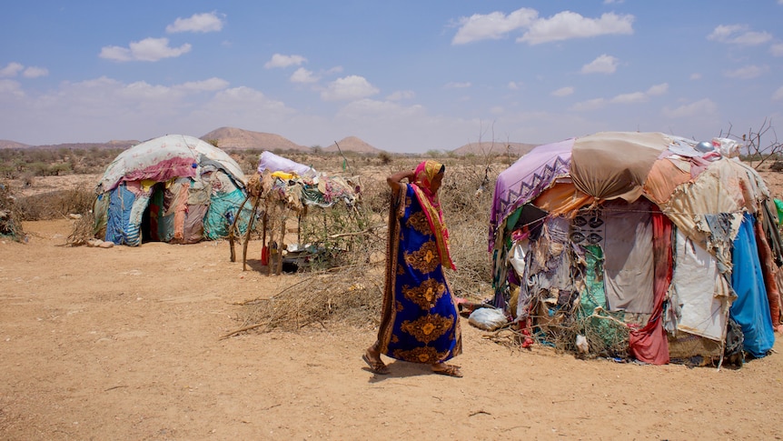 A woman in coloured clothes that cover her head and body walks past colourful tent homes made from pieces of fabric