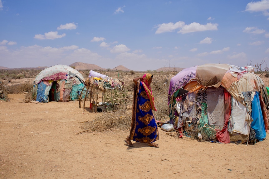 A woman in coloured clothes that cover her head and body walks past colourful tent homes made from pieces of fabric