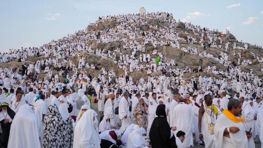 A large crowd of Muslims pilgrims wearing white gathered around a hill.