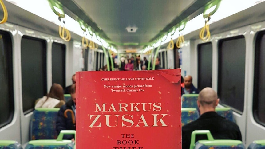 A hand holds a copy of The Book Thief inside a train.