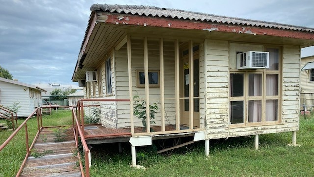 A decrepit small one-storey building with pale yellow paint peeling off 