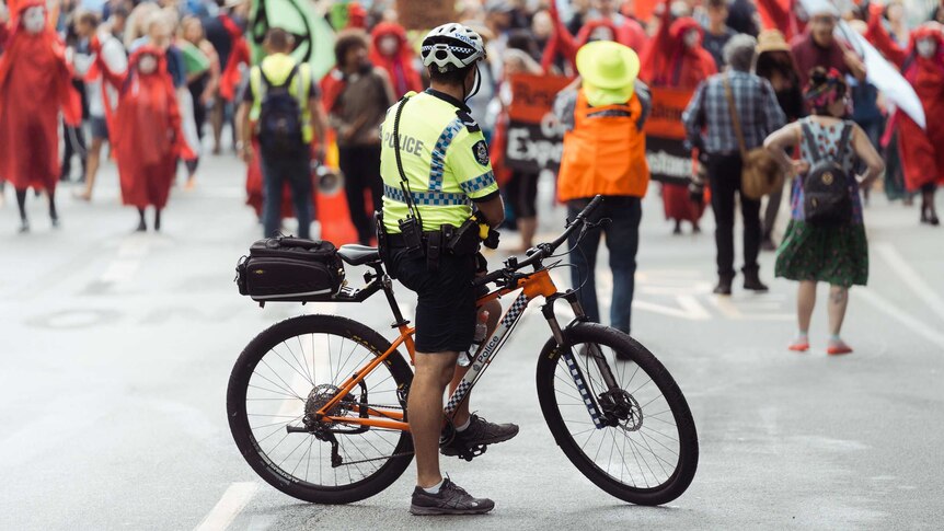 A police officer on a bike looks at a large group of protesters.
