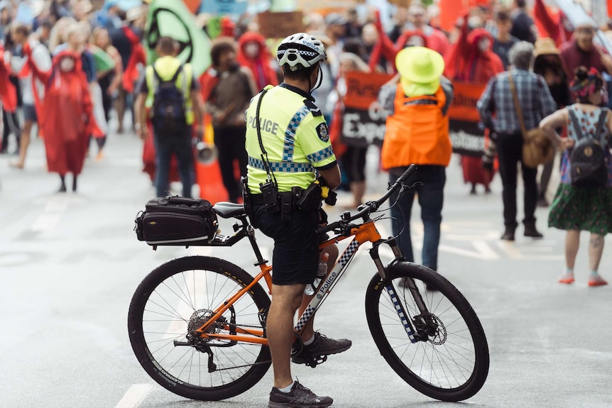 A police officer on a bike looks at a large group of protesters.